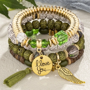 4-piece bohemian beaded bracelet set with green tassels and gold wing charms on stone surface