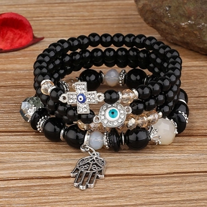 Close-up of multilayer beaded bracelet with Hamsa hand and evil eye charms on wood