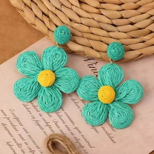 Close-up of handmade green and yellow raffia petal earrings on a vintage paper background