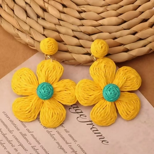 Detail of bohemian yellow and blue raffia flower earrings on a vintage paper background