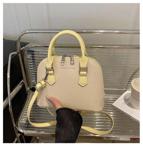 Close-up of light yellow shell bag with woven texture and Fashion & Bags metal logo