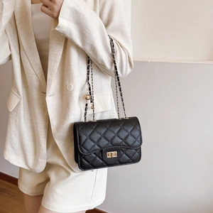 Sac bandoulière matelassé noir avec chaîne dorée et boule porté par un mannequin