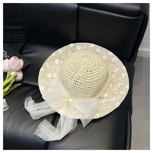 Close-up of straw hat with white floral lace embroidery and a beige tulle bow with pearls