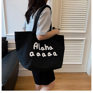 Detail of a large black canvas tote bag with white Alaha lettering shown from a side view