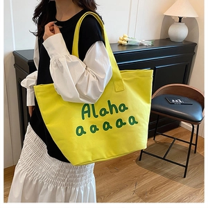 Detail of a bright yellow canvas tote bag with green letter print shown on a shoulder