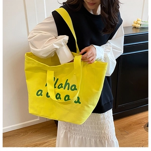 Detail of yellow canvas tote bag with green artistic lettering and dual strap design