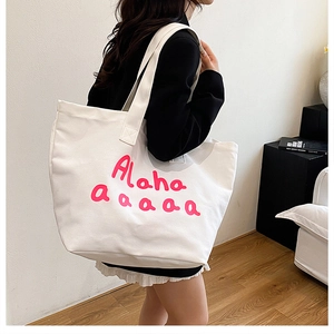 Side view of white canvas tote bag with pink Alaha text print and wide shoulder strap