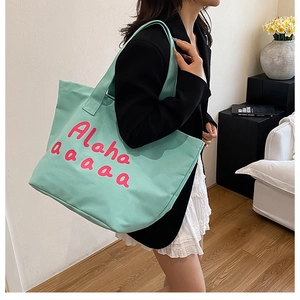 Detail of mint green canvas tote bag with pink Aloha lettering shown on model
