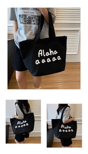 Detail of black canvas tote bag showing wide shoulder straps and white letter printing