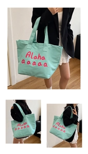 Detail view of mint green canvas tote bag featuring pink Alaha lettering and dual handles
