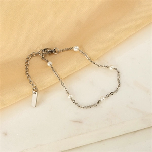 Minimalist stainless steel bracelet with five white pearls on champagne satin background