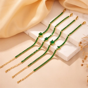 Close-up of four gold bracelets with green zircon stones on white marble background