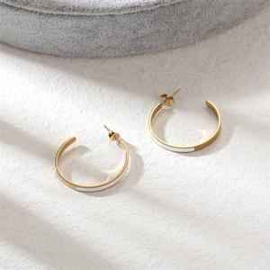 Golden C-shaped hoop earrings with white enamel finish on a minimalist white background