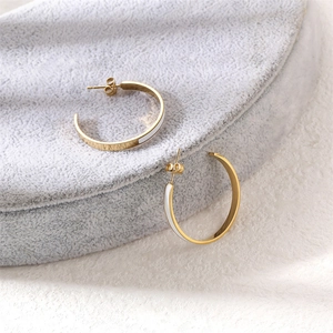 Minimalist gold-plated C-shaped earrings with white enamel stripes on a velvet stand