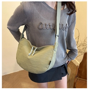 Detail of light green nylon crescent crossbody bag featuring adjustable wide strap and zipper