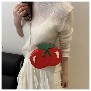 Detail of red cherry crossbody bag with green leaf accents and golden chain on model