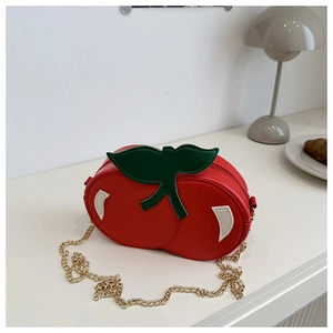 Detail of red cherry crossbody bag with green leaf accent and gold chain on table