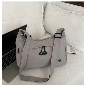 Dettaglio borsa a tracolla in nylon grigio con tasca laterale e zip su un letto bianco