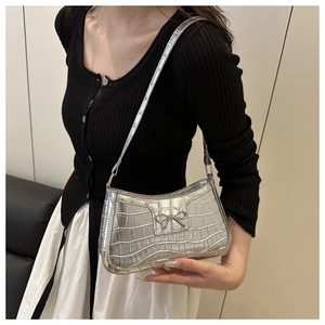 Silver crocodile pattern shoulder bag with a bow detail worn by a model in a side view