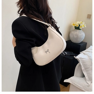 Detail van een beige halve maan hobo tas met een zilveren metalen strik op de schouder
