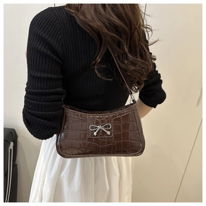 Detail of dark brown faux crocodile baguette bag with a silver bow clasp on shoulder