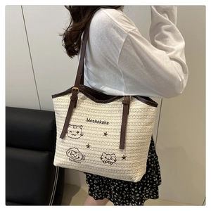 Detail of woven tote bag featuring cat embroidery, brown leather straps, and large capacity