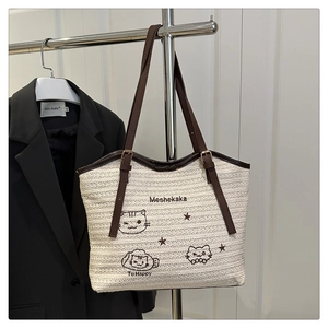 Detail of beige woven tote bag featuring cute cat embroidery and brown leather straps
