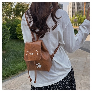 Outdoor view of a small brown PU leather backpack with a cute white cat face and paw print