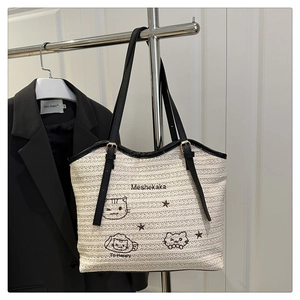 Detail of woven tote bag featuring cute cat embroidery and black leather shoulder straps