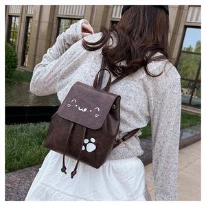 Outdoor view of a small brown leather backpack with cute white cat face and paw prints