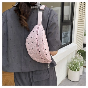 Pink pleated crossbody waist bag with black bow patterns and adjustable fabric strap
