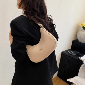 Minimalistische beige halve maan tas met zilveren strik gedragen op de schouder van model