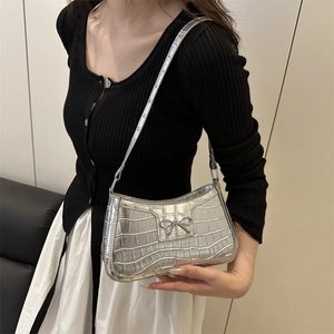 Sac sous le bras argenté motif crocodile avec nœud métallique porté par un mannequin