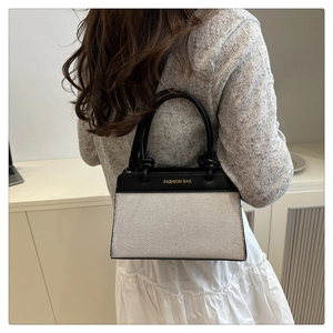 Detail of two-tone linen handbag featuring black leather handles and fashion bag logo