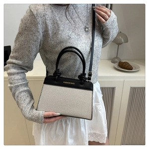 Detail of a minimalist linen handbag featuring contrast leather trim and crossbody strap