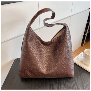 Detail of a large dark brown woven hobo tote bag on a dark wood surface