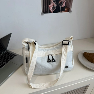 Detail of white nylon tote bag with black zippers and adjustable strap on a cafe table