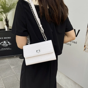White faux crocodile skin crossbody bag with silver chain worn by a model in black outfit