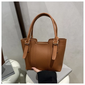Detailed macro of brown lychee grain leather tote bag with metal adjustment buckles