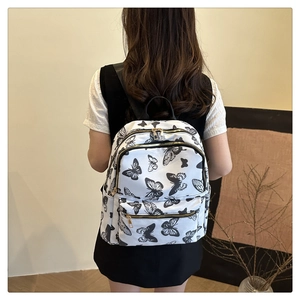 Detail of white butterfly print backpack featuring gold metal zippers and side pocket