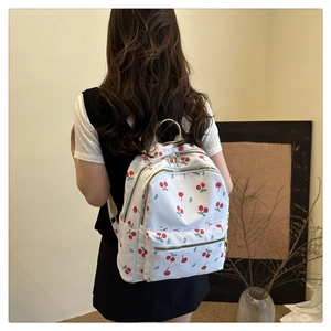 Detail of printed cherry backpack showing metal ring handle and silver zippers on white fabric