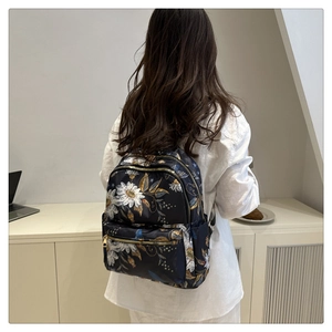 Close-up of floral print backpack with gold zippers worn by model in white shirt
