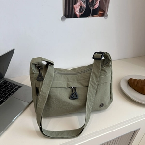 Sage green nylon tote bag featuring a front zipper pocket and adjustable strap detail