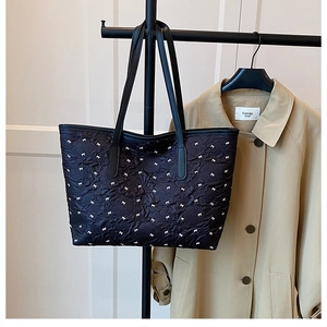 Detail view of black pleated tote bag with white bow print and leather shoulder straps