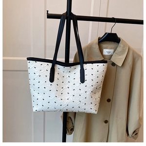 Detail of white textured tote bag with black bow patterns and contrast handles