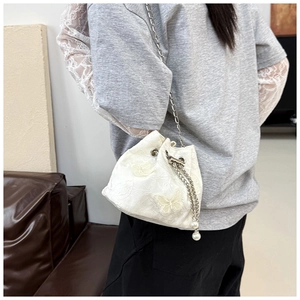 Close-up of white drawstring bucket bag with jacquard texture and 3D butterfly details