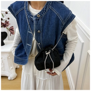 Detail of black embroidered bucket bag featuring pearl drawstring and silver chain strap