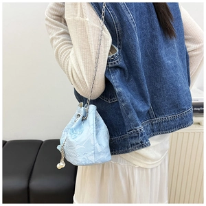 Detail of light blue embroidered bucket bag featuring embossed florals and pearl accents