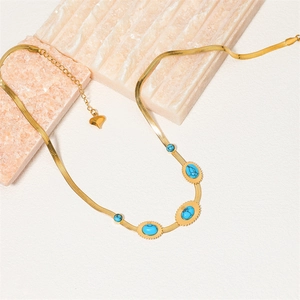Collana a catena piatta dorata con inserti in turchese e ciondolo a cuore su marmo
