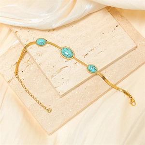 Dettaglio del bracciale a catena serpente dorata con pietre turchesi su marmo e seta